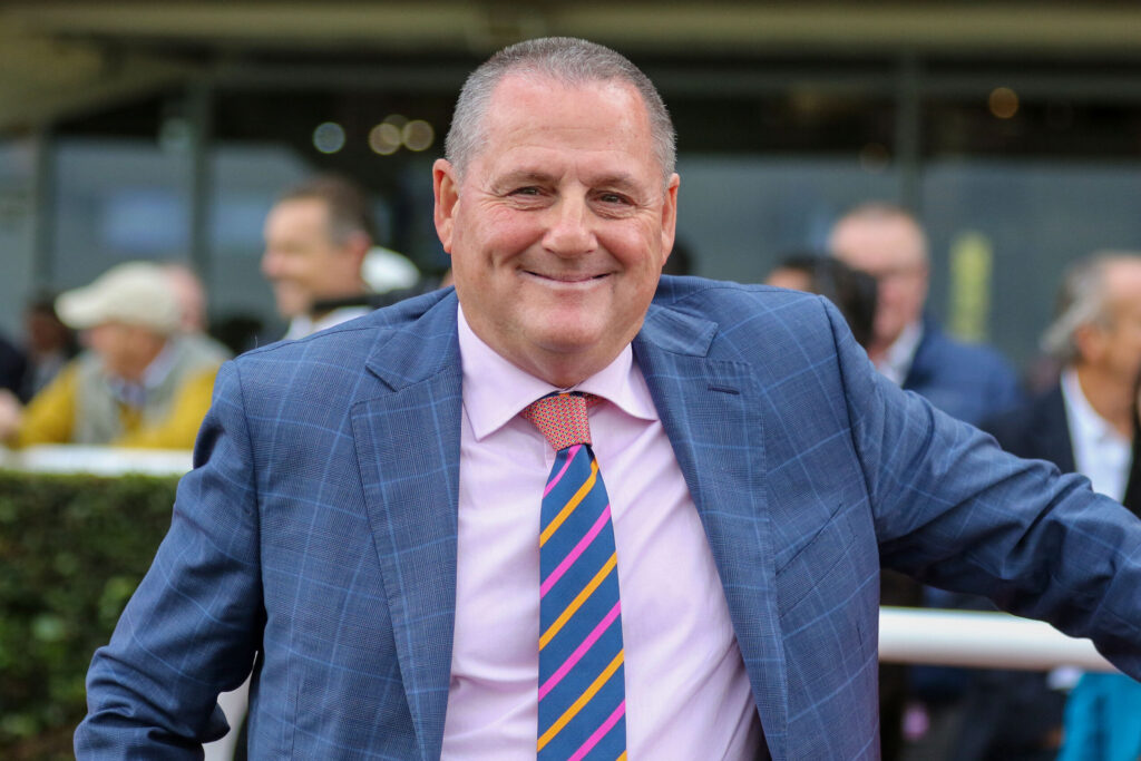 Smiling man in a blue plaid suit and pink shirt at an outdoor event, wearing a colorful striped tie.