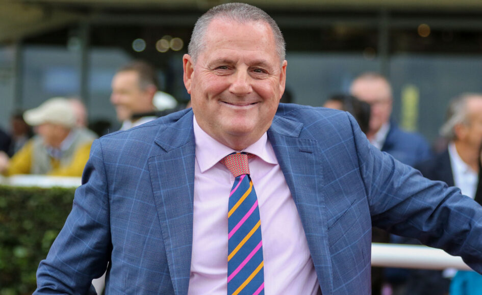 Smiling man in a blue plaid suit and pink shirt at an outdoor event, wearing a colorful striped tie.