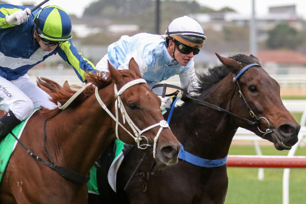 Two jockeys in colorful silks race side by side on fast-moving horses at a track.