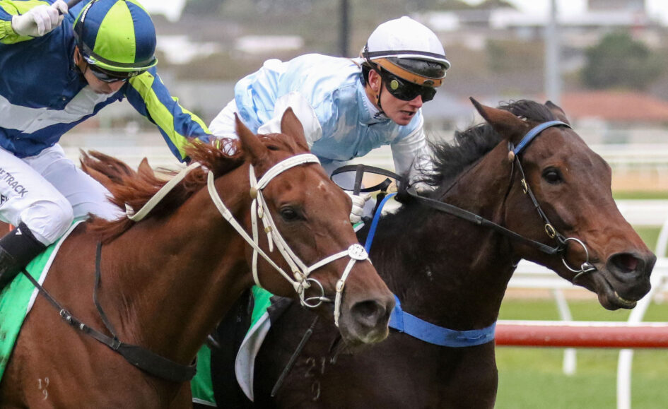 Two jockeys in colorful silks race side by side on fast-moving horses at a track.