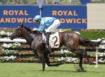 Jockey in blue silks riding a dark brown racehorse with number 2 on a track, Royal Randwick banners in the background.
