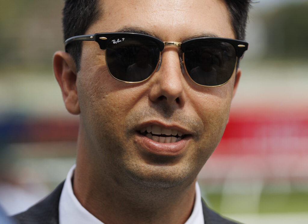 Close-up of a man wearing black Ray-Ban sunglasses and a suit outdoors.