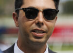 Close-up of a man wearing black Ray-Ban sunglasses and a suit outdoors.