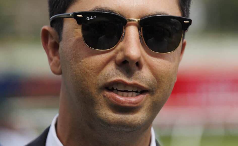 Close-up of a man wearing black Ray-Ban sunglasses and a suit outdoors.
