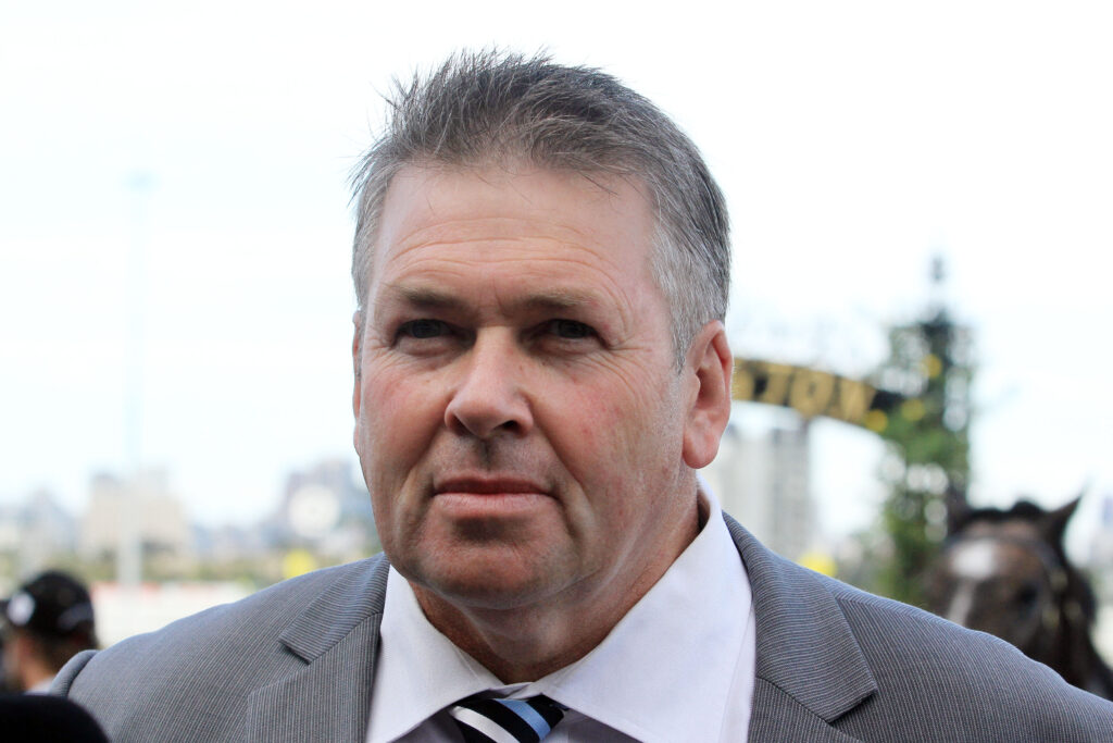 Close-up of a man in a gray suit and striped tie at an outdoor event with a blurred crowd in the background