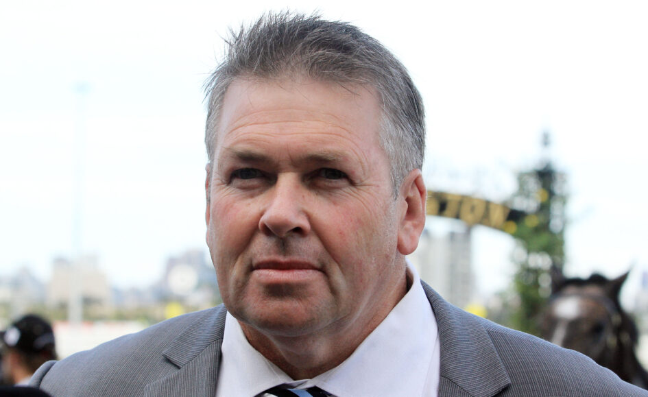 Close-up of a man in a gray suit and striped tie at an outdoor event with a blurred crowd in the background
