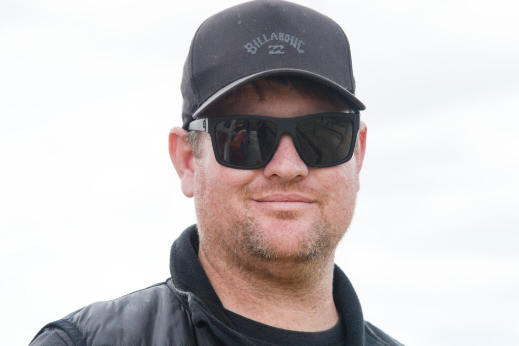 Close-up of a man wearing a black cap with a Billabong logo and dark sunglasses, outdoors against a bright sky.
