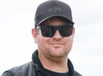 Close-up of a man wearing a black cap with a Billabong logo and dark sunglasses, outdoors against a bright sky.