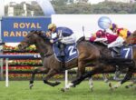 Leading horse and jockey in blue/yellow silks, wearing number 2, sprint toward the finish on a green racecourse.