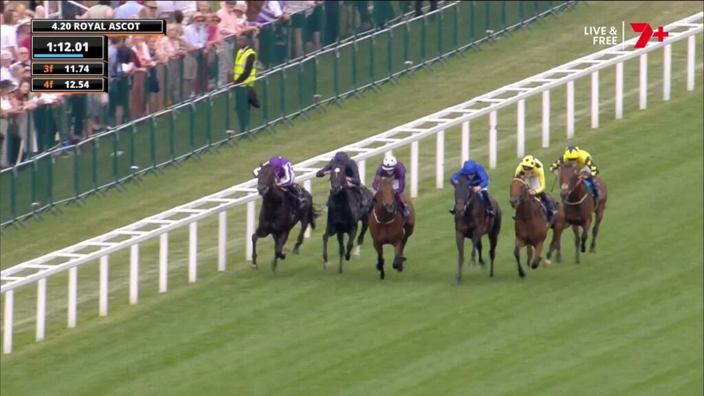 Royal Ascot horse race: jockeys in colorful silks gallop along a white railing with spectators watching.