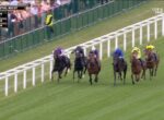 Royal Ascot horse race: jockeys in colorful silks gallop along a white railing with spectators watching.