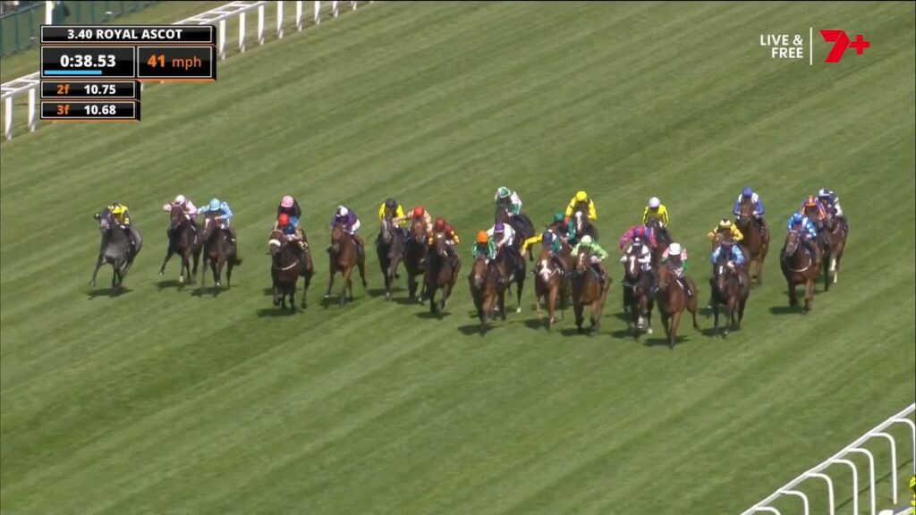 Pack of jockeys in bright silks riding Thoroughbreds on a green turf track at Royal Ascot; on-screen race clock and speed readout visible.