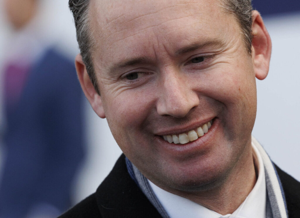 Close-up portrait of a smiling man looking slightly to the right, wearing a scarf and dark coat, showing teeth.
