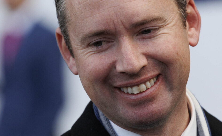Close-up portrait of a smiling man looking slightly to the right, wearing a scarf and dark coat, showing teeth.