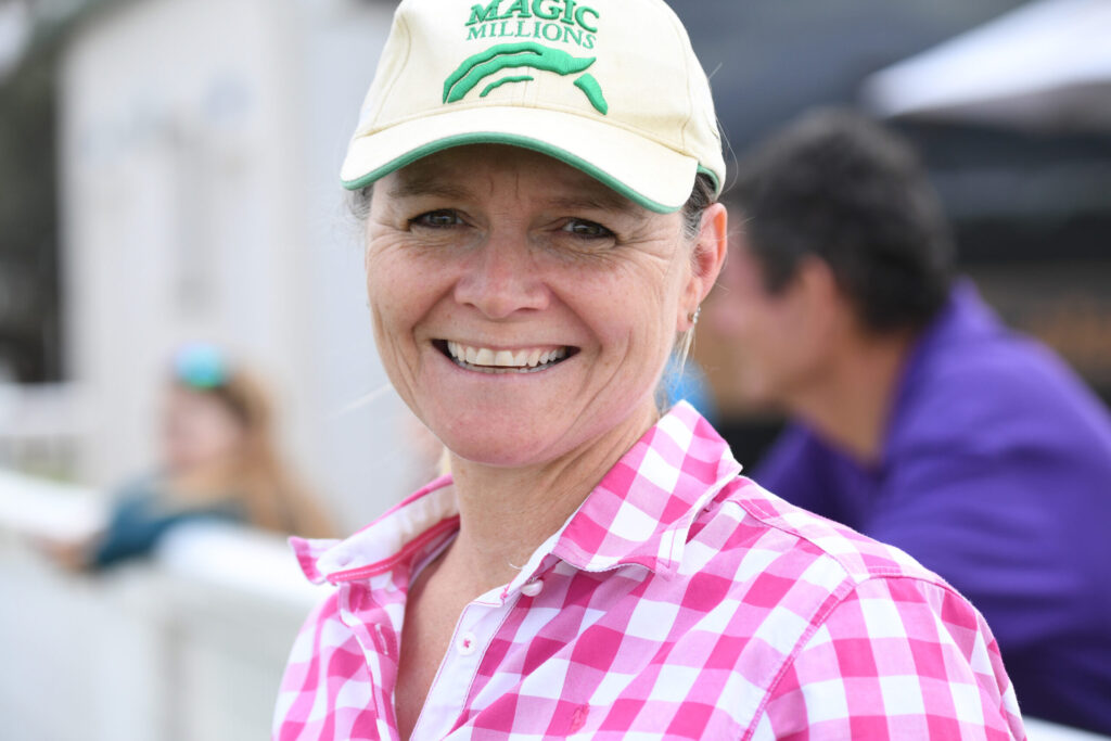 Smiling woman wearing a beige cap with a green logo and a pink checkered shirt, close-up outdoors.