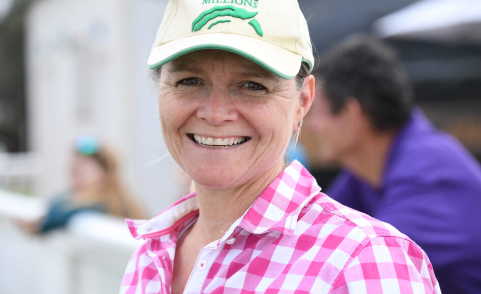 Smiling woman wearing a beige cap with a green logo and a pink checkered shirt, close-up outdoors.
