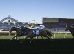 Horse race at Royal Randwick with jockeys in colorful silks charging down the turf, crowdless stands in the background.