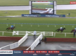 Horse race on turf at Sandown Hillside, blue-sleeved jockey leads a pack toward the finish with a large video screen in the background.