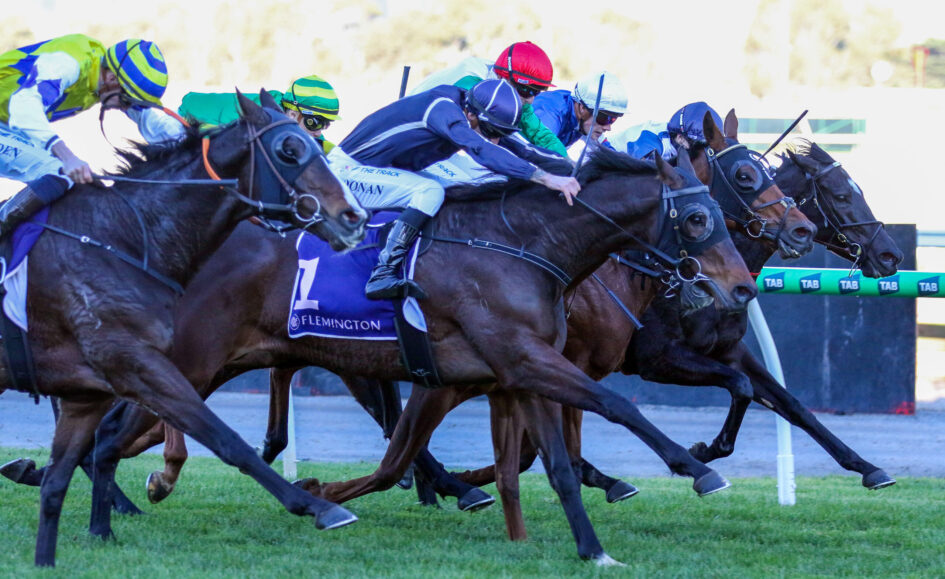 Group of jockeys in colorful silks racing side by side on galloping horses.