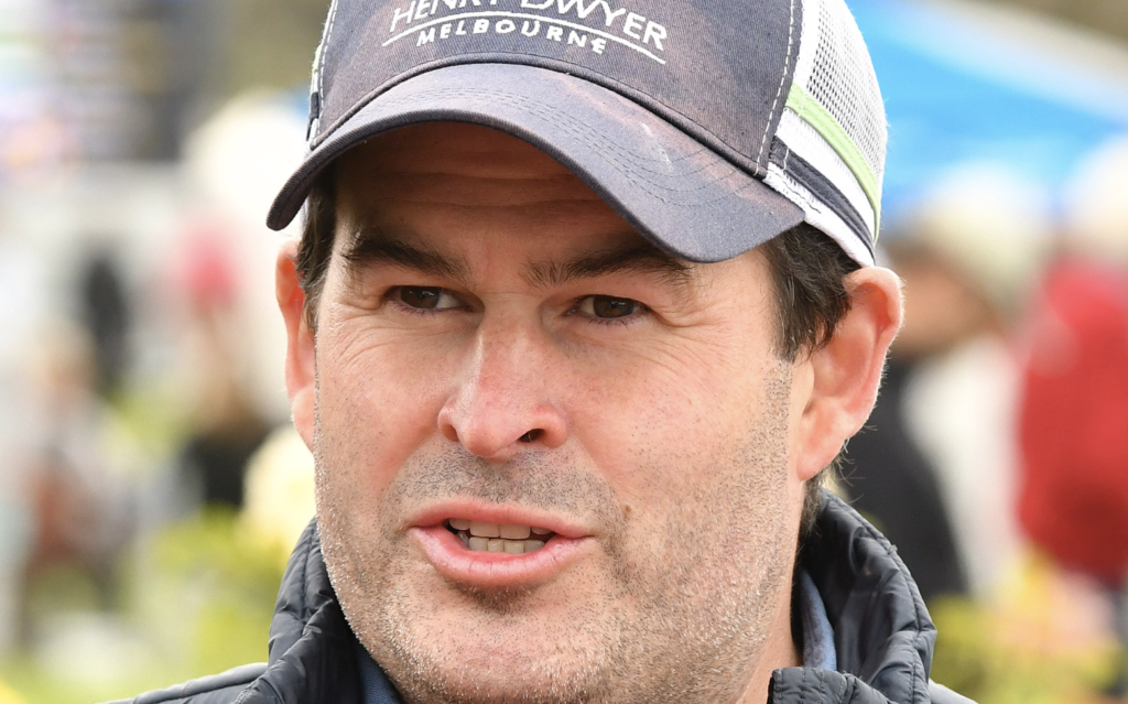 Close-up of a man wearing a gray cap and jacket, speaking outdoors.