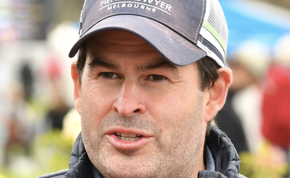 Close-up of a man wearing a gray cap and jacket, speaking outdoors.