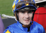 Close-up of a jockey wearing a blue and yellow helmet with goggles, facing the camera.