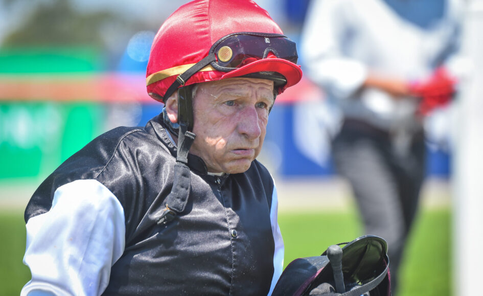 Older man wearing a red protective helmet and goggles, dressed in a black vest and white sleeves outdoors.