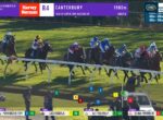 Horse race on a grass track with jockeys in colorful silks; banners show Harvey Norman R4 Canterbury 1900m at top-left/center