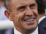 Close-up of a smiling man in a dark suit and white shirt, showing teeth.