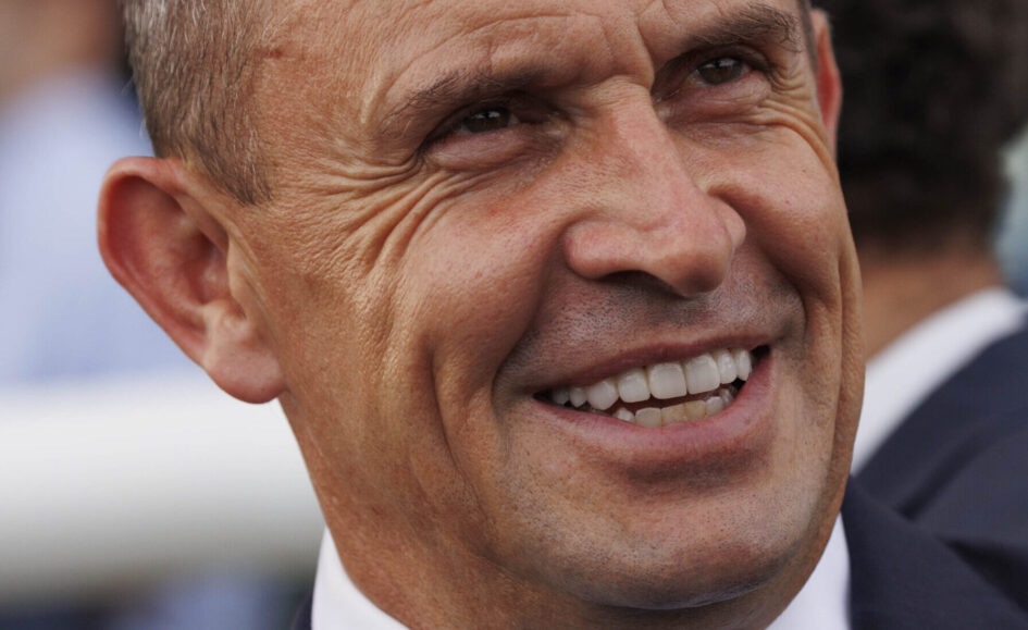 Close-up of a smiling man in a dark suit and white shirt, showing teeth.