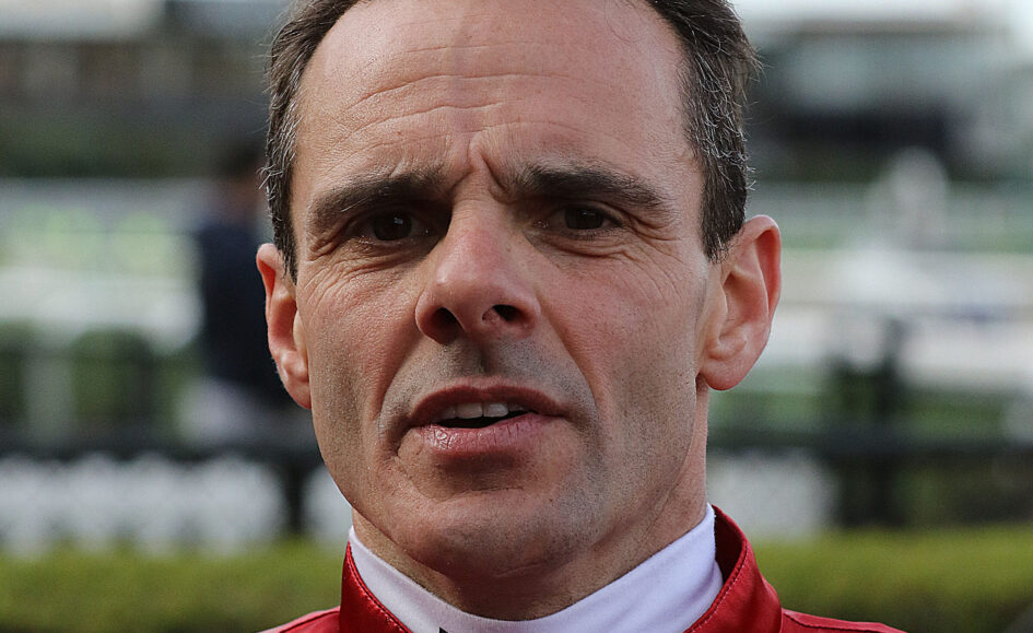 Close-up portrait of a man in a red racing jacket outdoors, focusing on his face from the nose up.