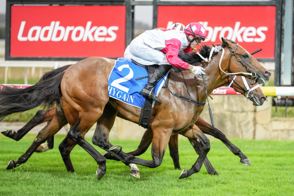 Two jockeys on brown horses sprint neck-and-neck on a green turf, with a red Ladbrokes sign in the background.