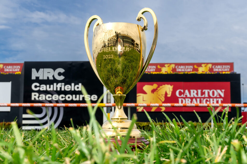 Gold trophy on a podium at a racecourse, with Carlton Draught banners and a blue sky in the background. Grass is in the foreground.